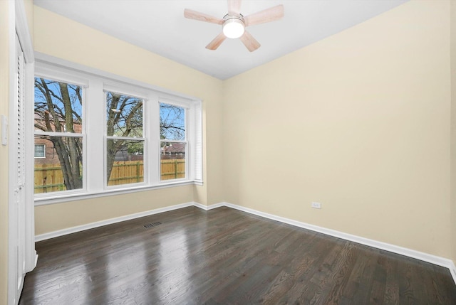spare room with baseboards, a ceiling fan, dark wood-style floors, and visible vents