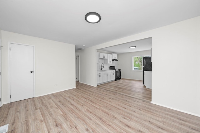 unfurnished living room featuring light wood-style floors, a sink, and baseboards
