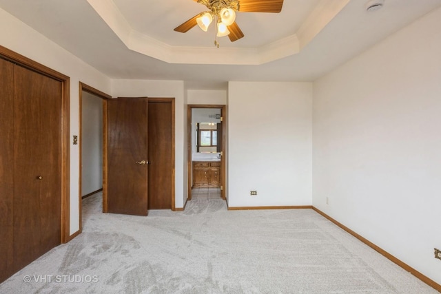 unfurnished bedroom with a tray ceiling, light carpet, baseboards, and ensuite bath