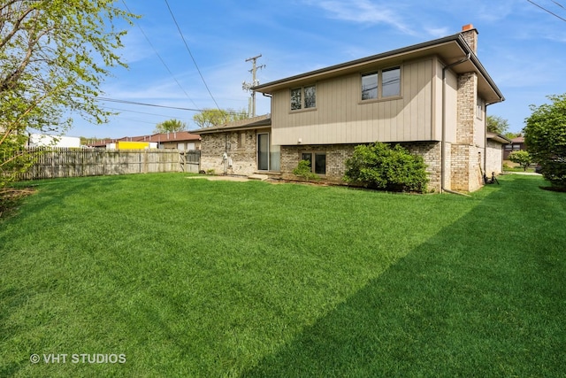 back of property featuring brick siding, fence, a yard, and a chimney