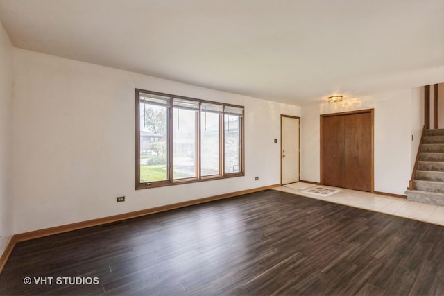 unfurnished living room featuring baseboards, stairs, and wood finished floors
