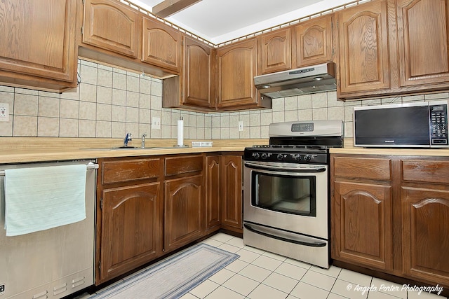 kitchen with light countertops, under cabinet range hood, light tile patterned flooring, and stainless steel appliances