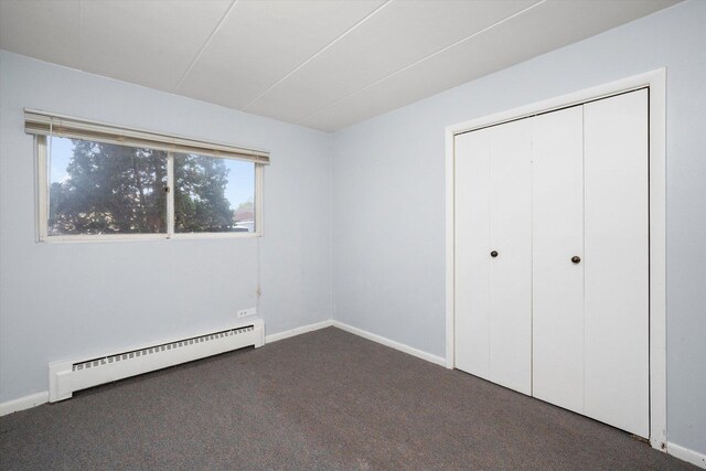 unfurnished bedroom featuring dark carpet, baseboards, and a baseboard heating unit