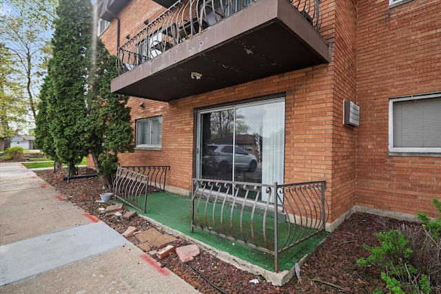 entrance to property featuring brick siding, fence, and a balcony