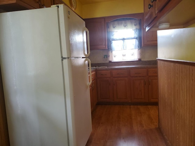 kitchen featuring brown cabinetry, freestanding refrigerator, wood finished floors, and dark countertops