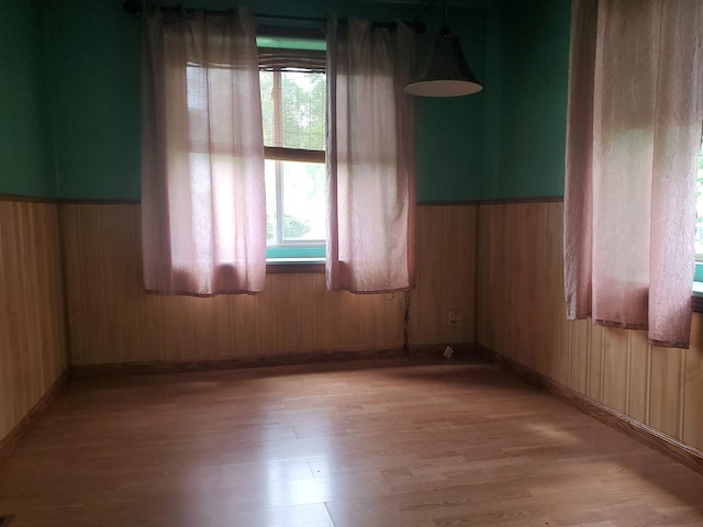 spare room with baseboards, wood walls, light wood finished floors, and a wainscoted wall