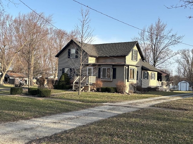 view of front facade featuring driveway, a front yard, an outbuilding, a storage unit, and a shingled roof