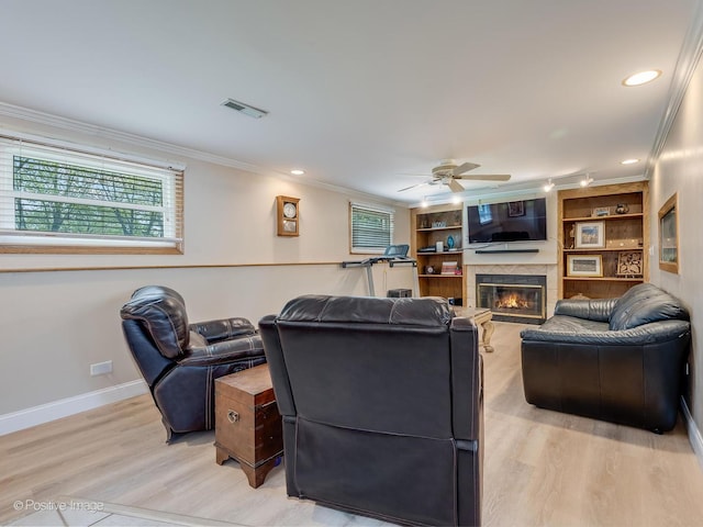 living room featuring ceiling fan, visible vents, a glass covered fireplace, light wood-style floors, and ornamental molding