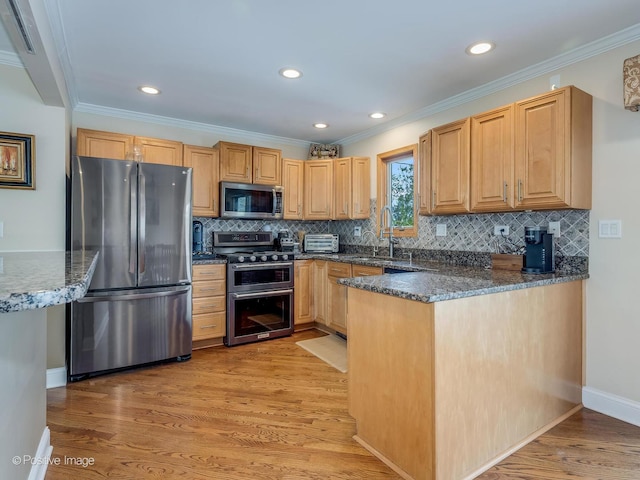kitchen with appliances with stainless steel finishes, light wood-type flooring, a sink, dark stone counters, and ornamental molding