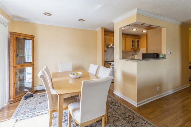 dining area featuring light wood-type flooring, baseboards, crown molding, and baseboard heating