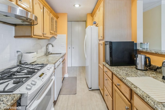 kitchen with a sink, under cabinet range hood, white appliances, and light stone countertops