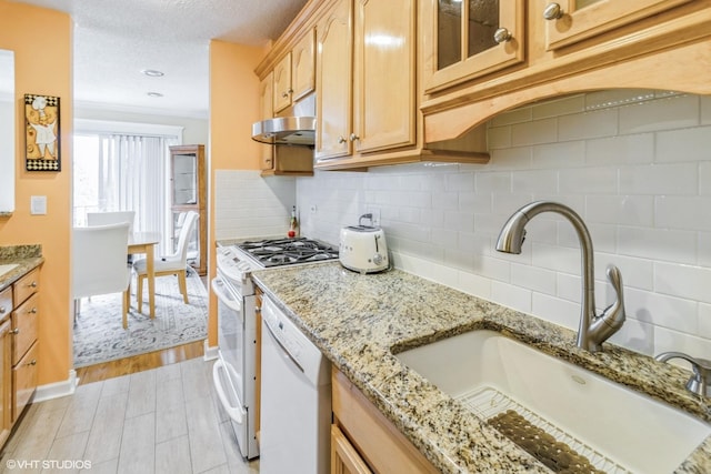 kitchen with white dishwasher, a sink, decorative backsplash, under cabinet range hood, and range with gas cooktop