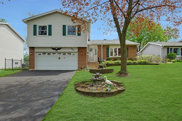 tri-level home featuring fence, a front yard, brick siding, an attached garage, and driveway