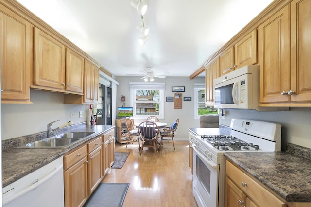 kitchen featuring white appliances, dark countertops, a sink, and light wood finished floors