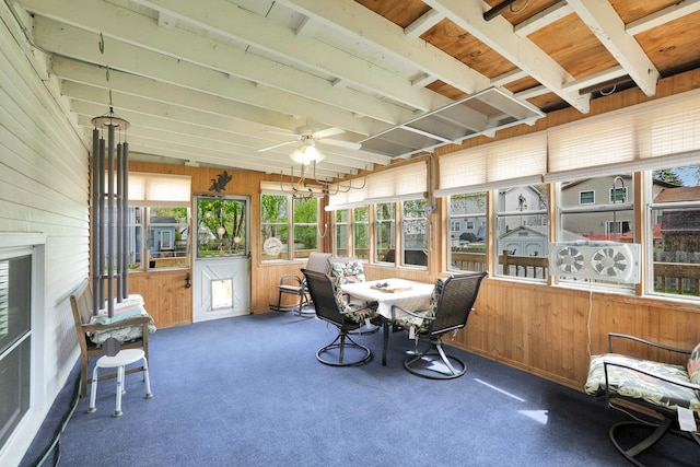 sunroom with wooden walls, a ceiling fan, and carpet flooring