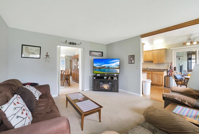 living room featuring light colored carpet, a ceiling fan, baseboards, and a glass covered fireplace