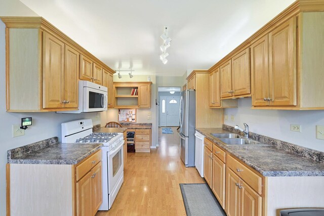 kitchen with light wood-style floors, a sink, dark countertops, and white appliances
