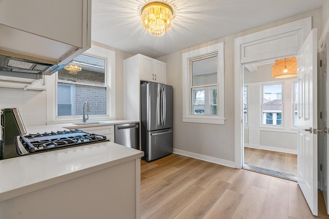 kitchen with light wood-type flooring, light countertops, a sink, appliances with stainless steel finishes, and a notable chandelier