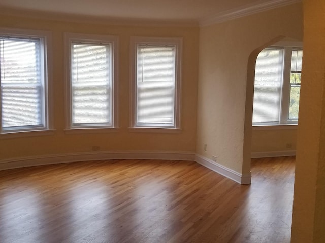 spare room with crown molding, arched walkways, baseboards, and wood finished floors