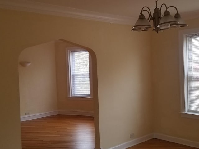 spare room with arched walkways, an inviting chandelier, a wealth of natural light, and wood finished floors