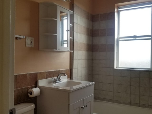 bathroom with toilet, tile walls, plenty of natural light, and vanity