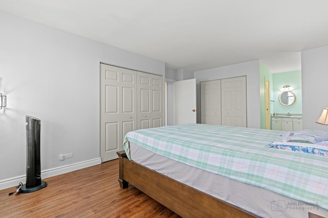 bedroom featuring baseboards, ensuite bathroom, wood finished floors, and two closets