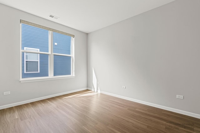 unfurnished room featuring baseboards, wood finished floors, and visible vents