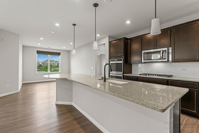 kitchen featuring dark brown cabinetry, dark wood-type flooring, tasteful backsplash, a sink, and appliances with stainless steel finishes
