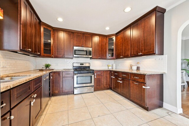kitchen featuring tasteful backsplash, arched walkways, light stone counters, stainless steel appliances, and light tile patterned floors