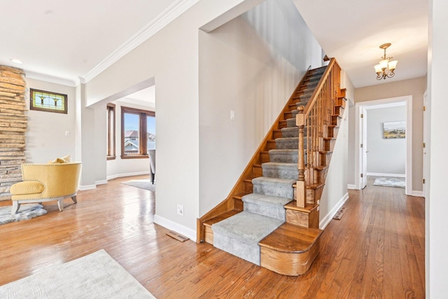 staircase with wood finished floors, crown molding, a chandelier, and baseboards