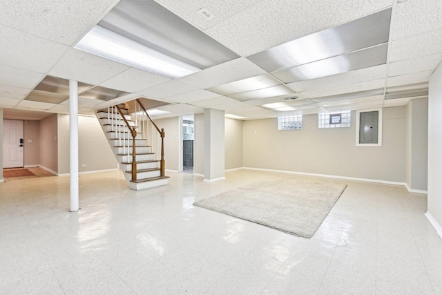 basement with stairway, a paneled ceiling, electric panel, and baseboards