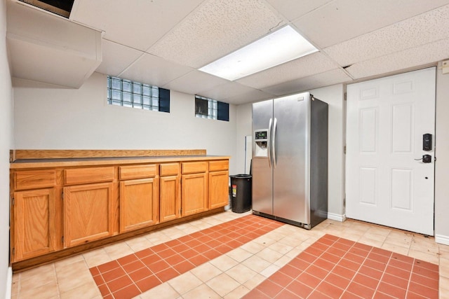kitchen featuring light tile patterned floors, stainless steel fridge, light countertops, brown cabinets, and a paneled ceiling