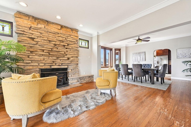 living area featuring wood finished floors, a healthy amount of sunlight, a stone fireplace, and crown molding