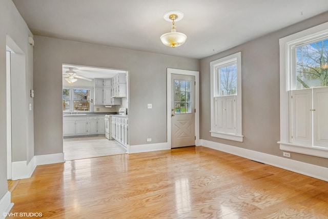 unfurnished dining area featuring a ceiling fan, baseboards, a sink, and light wood-type flooring
