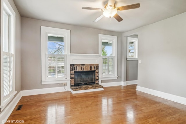 unfurnished living room featuring visible vents, a glass covered fireplace, wood finished floors, baseboards, and a ceiling fan