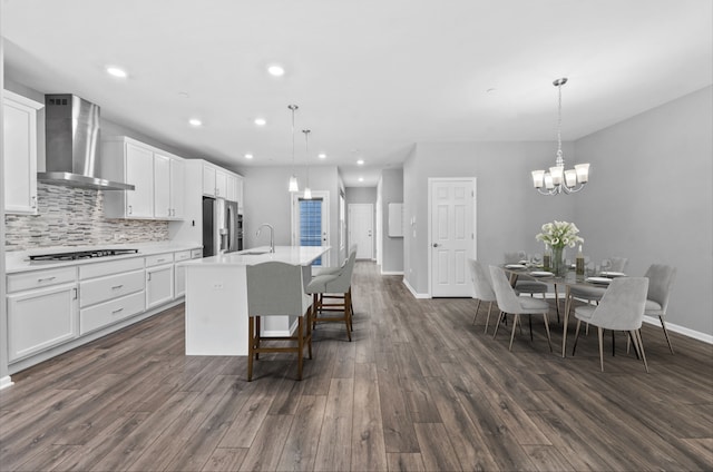 kitchen featuring wall chimney range hood, a notable chandelier, a sink, cooktop, and stainless steel refrigerator with ice dispenser