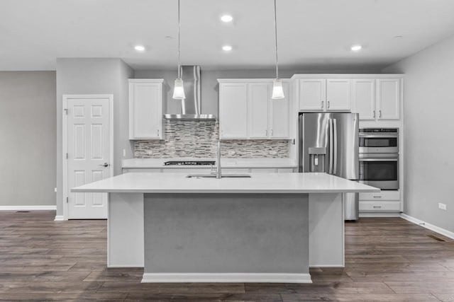 kitchen with a center island with sink, a sink, light countertops, white cabinets, and wall chimney exhaust hood
