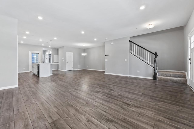 unfurnished living room featuring baseboards, dark wood finished floors, stairway, and an inviting chandelier