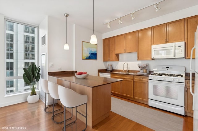 kitchen with white appliances, dark countertops, a sink, and brown cabinets
