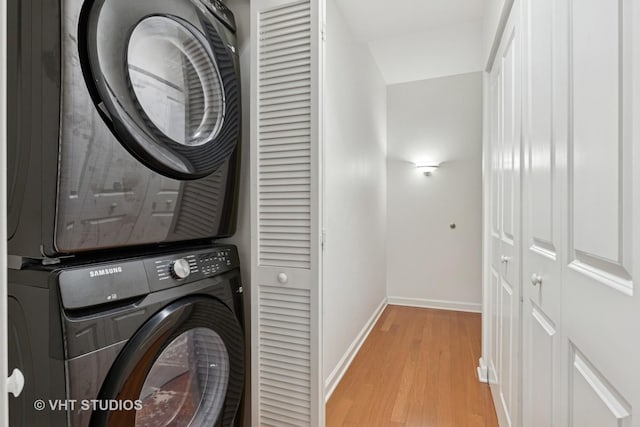 clothes washing area with stacked washer / dryer, baseboards, and light wood finished floors
