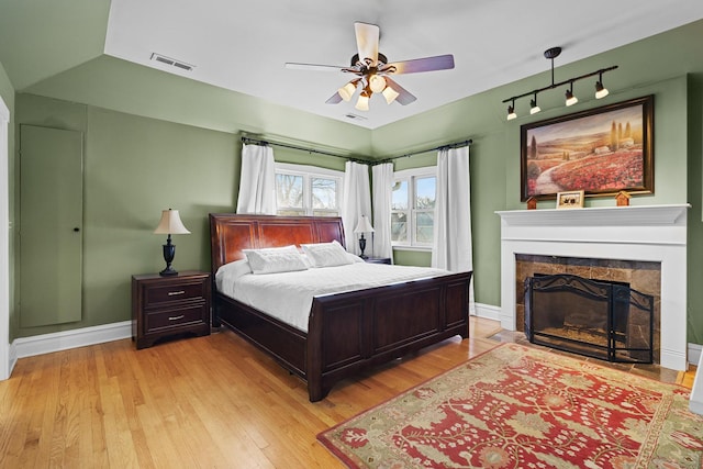 bedroom with light wood-type flooring, track lighting, visible vents, a stone fireplace, and baseboards