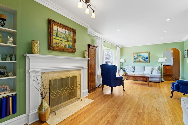 living area featuring arched walkways, ornamental molding, light wood finished floors, a premium fireplace, and built in features