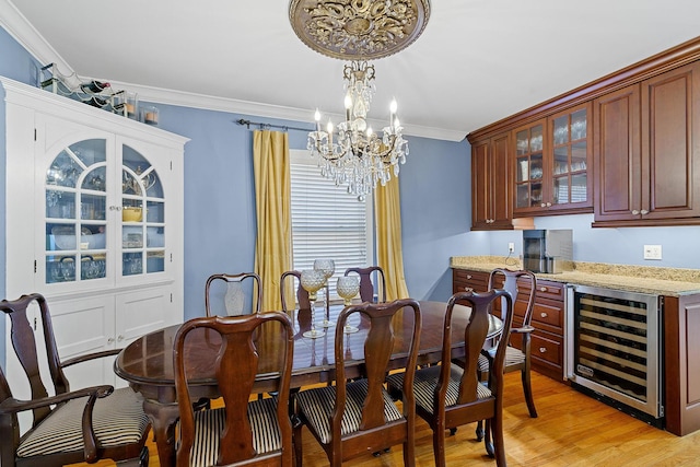 dining space featuring light wood finished floors, an inviting chandelier, wine cooler, bar area, and ornamental molding
