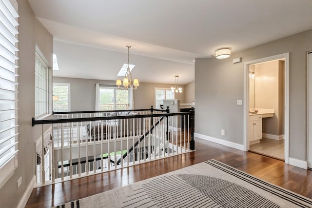 hall with baseboards, wood finished floors, a notable chandelier, and an upstairs landing