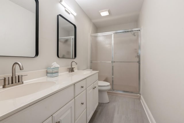 bathroom featuring double vanity, a sink, toilet, and a shower stall