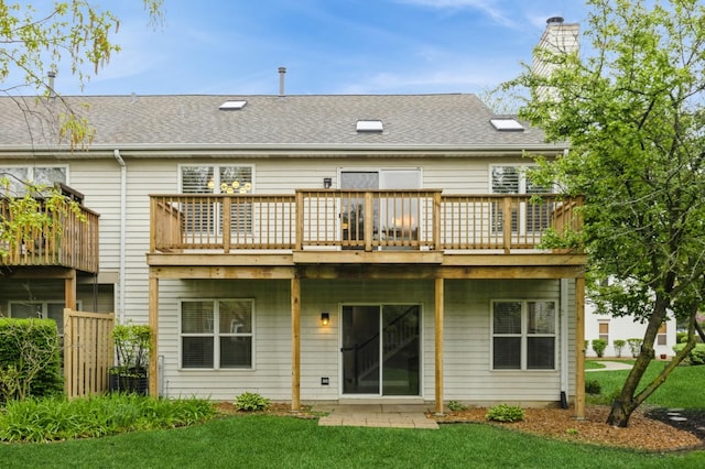 rear view of property featuring a lawn, a shingled roof, and a wooden deck