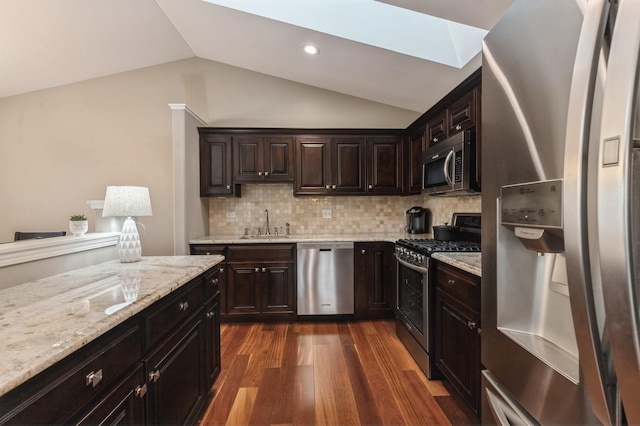 kitchen with light stone counters, a sink, stainless steel appliances, dark wood-type flooring, and vaulted ceiling