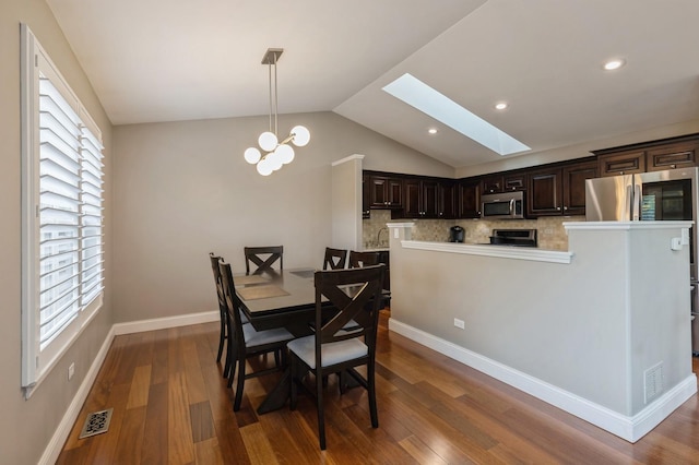 dining room with visible vents, lofted ceiling with skylight, plenty of natural light, a chandelier, and dark wood finished floors