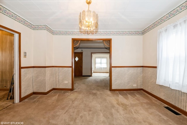 carpeted spare room with an inviting chandelier and visible vents