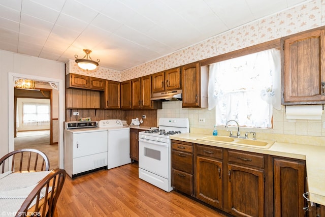 kitchen with a sink, white range with gas cooktop, tasteful backsplash, under cabinet range hood, and washing machine and dryer